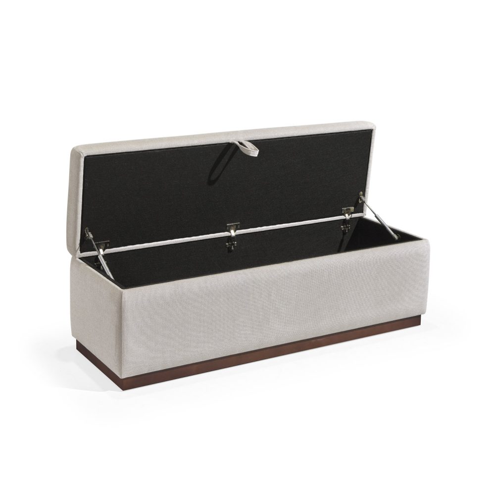 Banqueta retangular com topo almofadado, revestido em tecido bege, com uma base de madeira. Inclui um puxador em tecido na parte frontal para abrir o compartimento interno de arrumação, combinando funcionalidade e estilo.