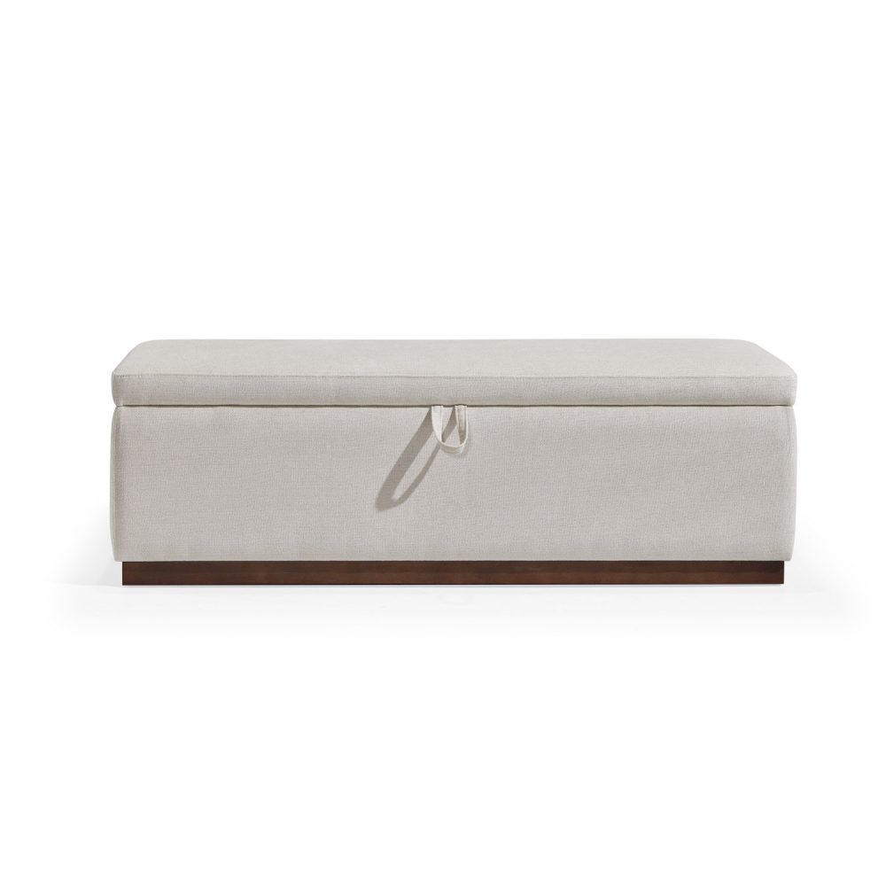Banqueta retangular com topo almofadado, revestido em tecido bege, com uma base de madeira. Inclui um puxador em tecido na parte frontal para abrir o compartimento interno de arrumação, combinando funcionalidade e estilo.