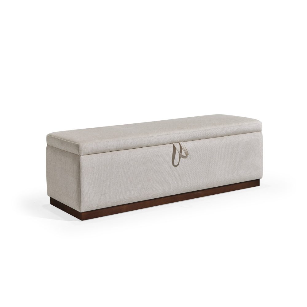 Banqueta retangular com topo almofadado, revestido em tecido bege, com uma base de madeira. Inclui um puxador em tecido na parte frontal para abrir o compartimento interno de arrumação, combinando funcionalidade e estilo.