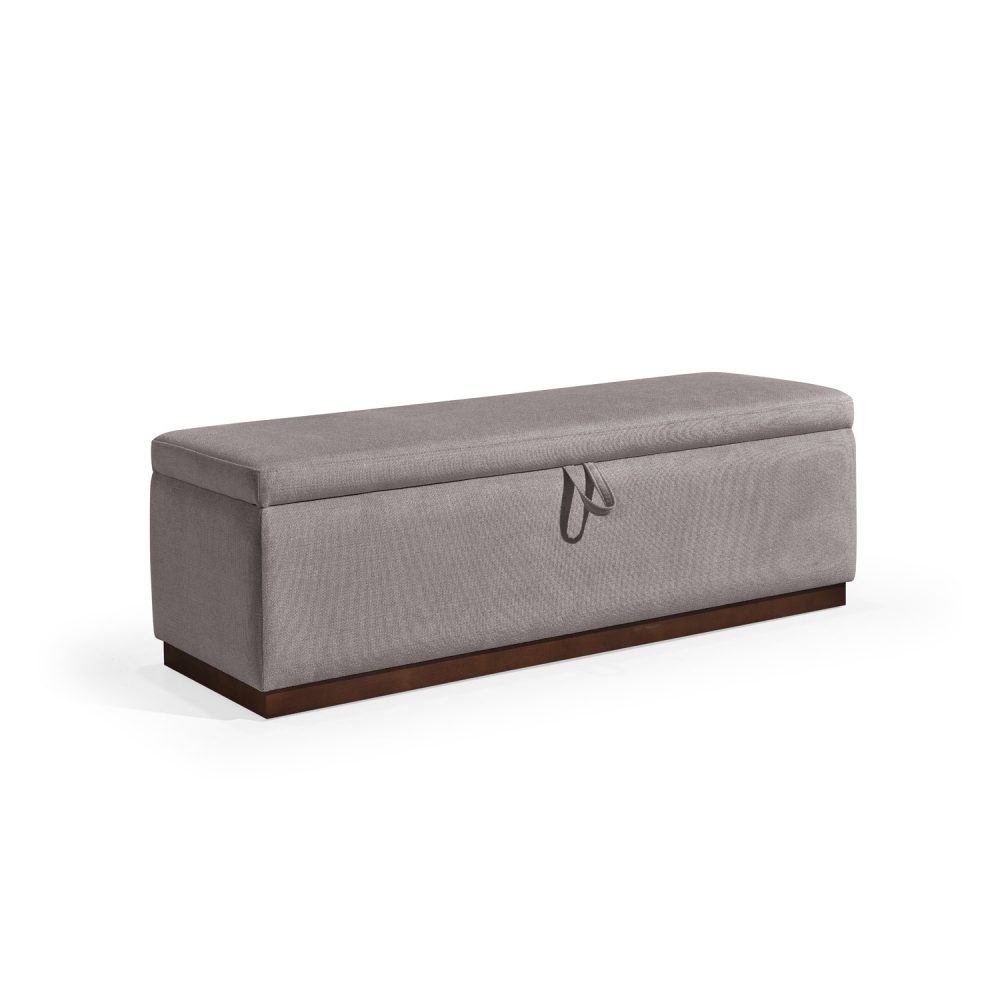 Banqueta retangular com topo almofadado, revestido em tecido cinza, com uma base de madeira. Inclui um puxador em tecido na parte frontal para abrir o compartimento interno de arrumação, combinando funcionalidade e estilo.