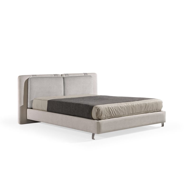 Cama moderna com cabeceira almofadada em tecido cinza-claro, composta por duas grandes almofadas anexadas. A estrutura da cama é estofada no mesmo tecido cinza-claro, com lençóis bege e cobertor cinza-escuro. A cama possui pés metálicos elegantes que a elevam ligeiramente do chão