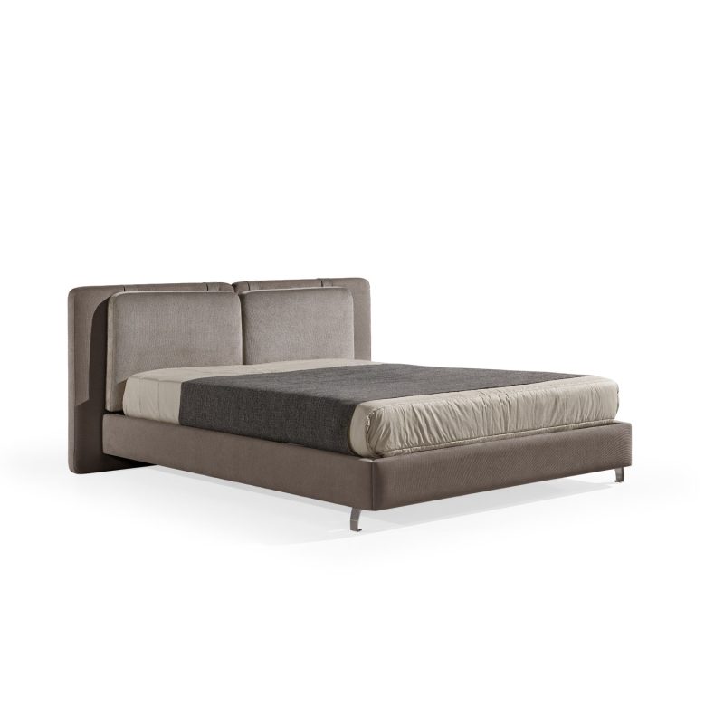Cama moderna com cabeceira almofadada em tecido castanho, composta por duas grandes almofadas anexadas. A estrutura da cama é estofada no mesmo tecido castanho, com lençóis bege e cobertor cinza-escuro. A cama possui pés metálicos elegantes que a elevam ligeiramente do chão