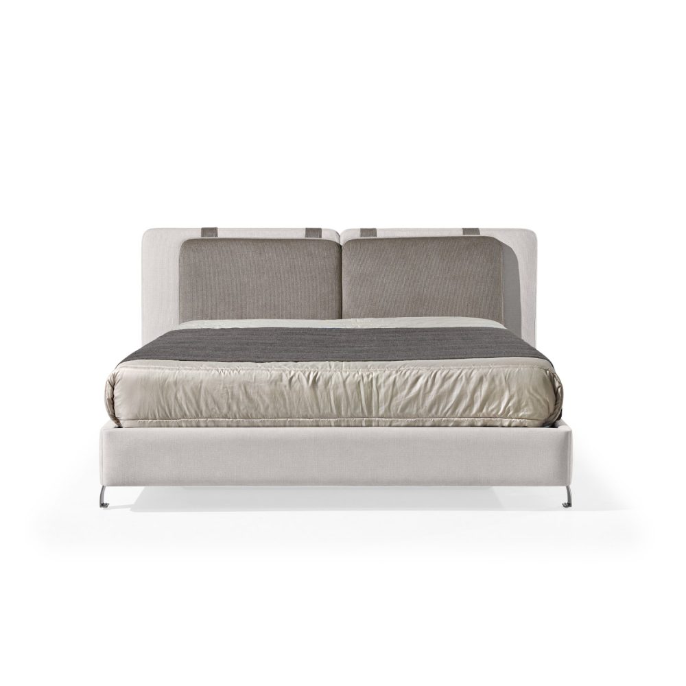 Cama moderna com cabeceira almofadada em tecido cinza-claro, composta por duas grandes almofadas anexadas. A estrutura da cama é estofada no mesmo tecido cinza-claro, com lençóis bege e cobertor cinza-escuro. A cama possui pés metálicos elegantes que a elevam ligeiramente do chão