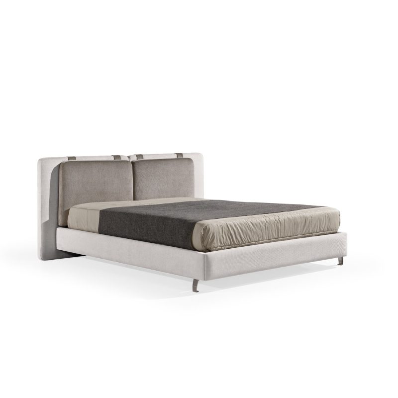 Cama moderna com cabeceira almofadada em tecido cinza-claro, composta por duas grandes almofadas anexadas. A estrutura da cama é estofada no mesmo tecido cinza-claro, com lençóis bege e cobertor cinza-escuro. A cama possui pés metálicos elegantes que a elevam ligeiramente do chão
