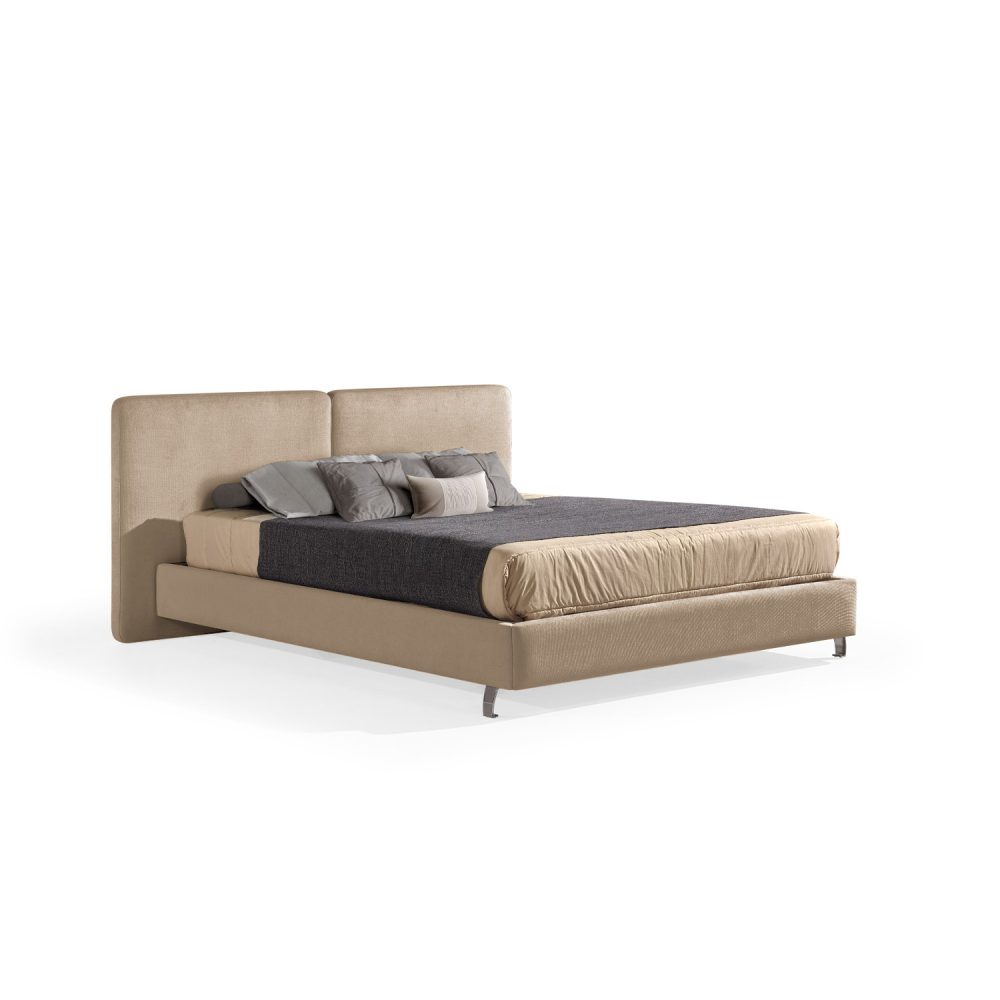 Cama moderna com cabeceira acolchoada de grandes dimensões, estrutura baixa em amarelo, colchão bege e roupa de cama com cobertor cinza-escuro e almofadas em tons de bege e cinza. A cama tem pés metálicos pequenos que conferem um design elegante e contemporâneo.