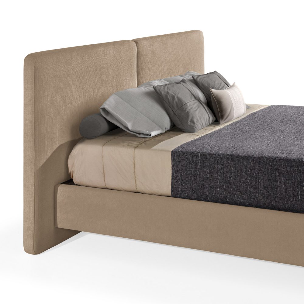 Cama moderna com cabeceira acolchoada de grandes dimensões, estrutura baixa em amarelo, colchão bege e roupa de cama com cobertor cinza-escuro e almofadas em tons de bege e cinza. A cama tem pés metálicos pequenos que conferem um design elegante e contemporâneo.