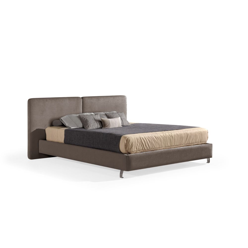 Cama moderna com cabeceira acolchoada de grandes dimensões, estrutura baixa castanho, colchão bege e roupa de cama com cobertor cinza-escuro e almofadas em tons de bege e cinza. A cama tem pés metálicos pequenos que conferem um design elegante e contemporâneo.