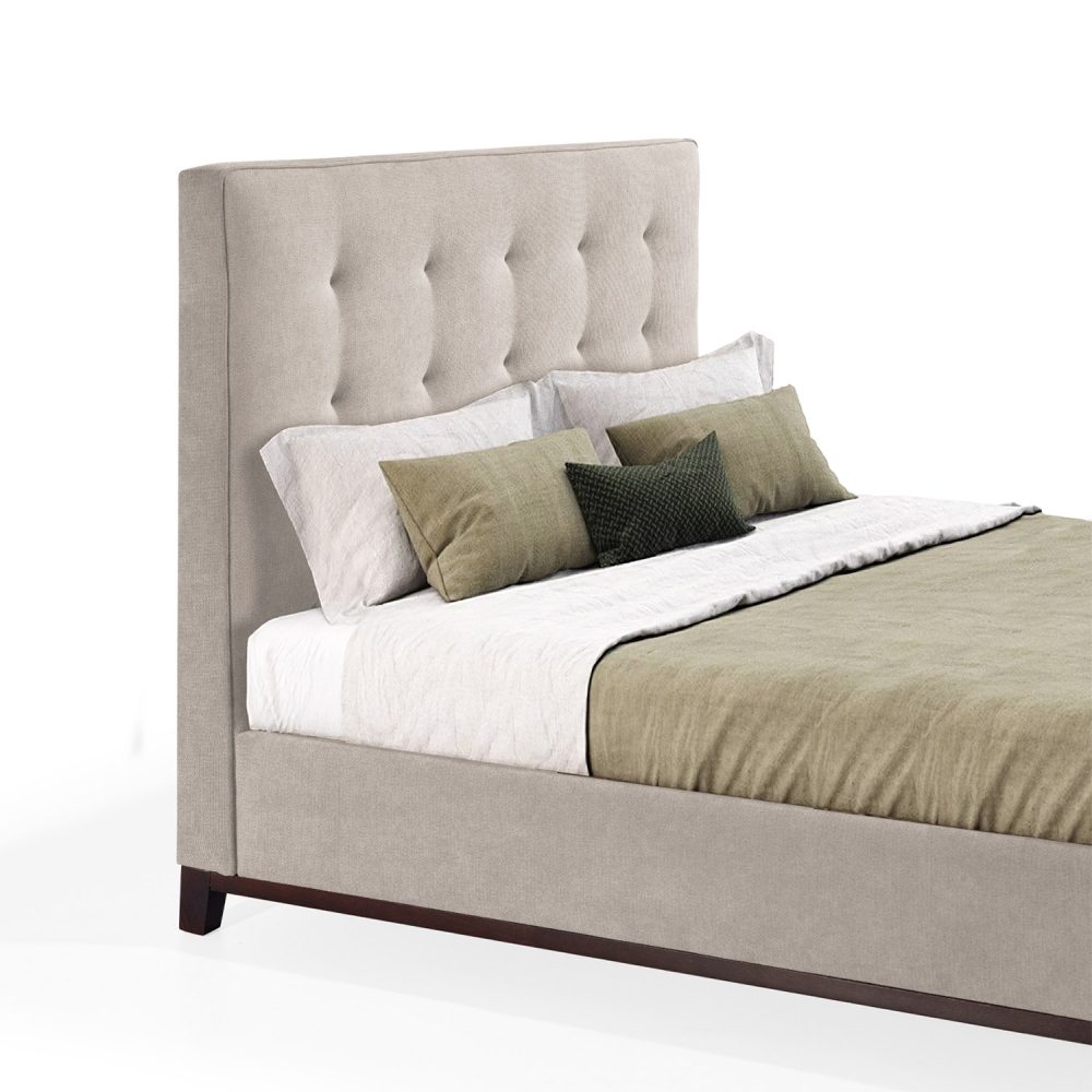 Cama moderna com cabeceira acolchoada e estofada em tecido bege, com lençóis brancos, uma manta verde e várias almofadas em tons de verde e branco. A estrutura da cama é revestida com tecido bege e possui pés de madeira escura.