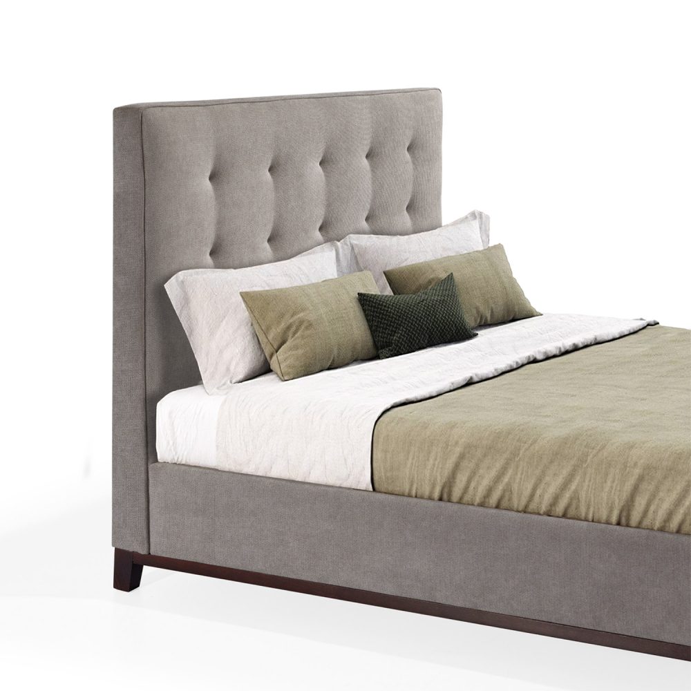 Cama moderna com cabeceira acolchoada e estofada em tecido bege, com lençóis brancos, uma manta verde e várias almofadas em tons de verde e branco. A estrutura da cama é revestida com tecido bege e possui pés de madeira escura.