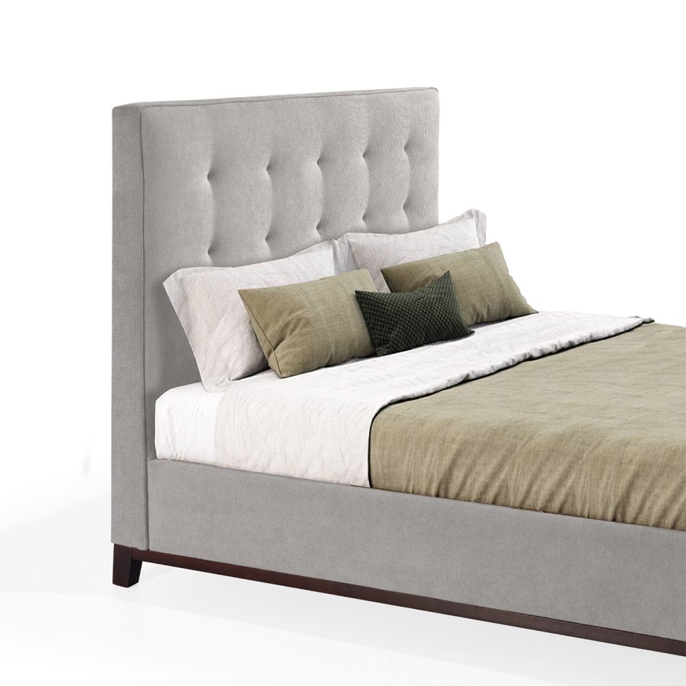 Cama moderna com cabeceira acolchoada e estofada em tecido bege, com lençóis brancos, uma manta verde e várias almofadas em tons de verde e branco. A estrutura da cama é revestida com tecido bege e possui pés de madeira escura.