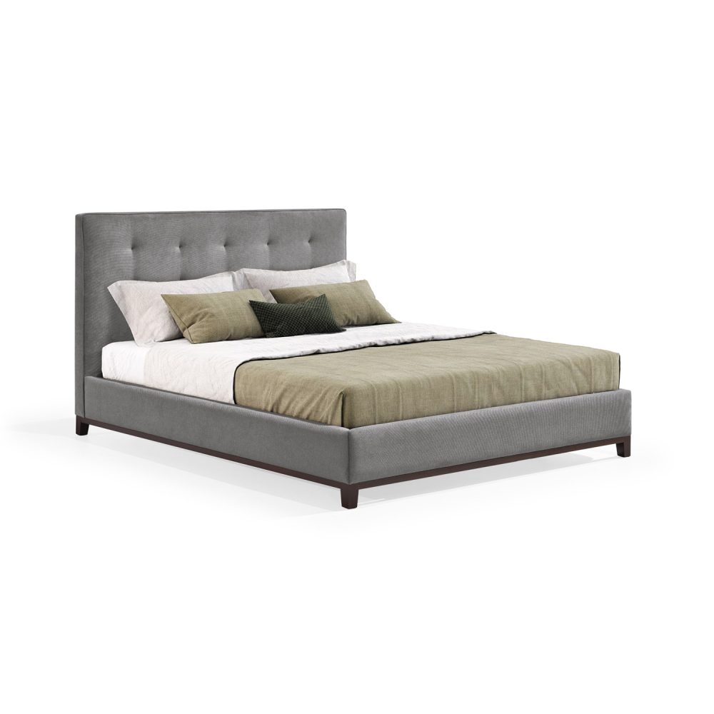 Cama moderna com cabeceira acolchoada e estofada em tecido cinza, com lençóis brancos, uma manta verde e várias almofadas em tons de verde e branco. A estrutura da cama é revestida com tecido cinza e possui pés de madeira escura.