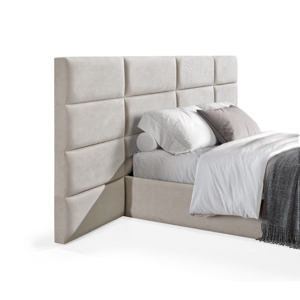 Cama moderna com cabeceira acolchoada em branco, lençóis brancos, cobertor cinzento e várias almofadas em tons de cinza e branco, com estrutura estofada no mesmo tecido cinzento.