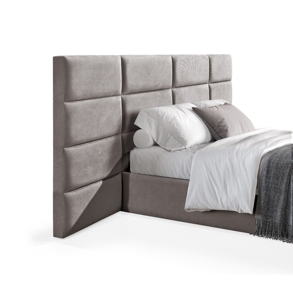 Cama moderna com cabeceira acolchoada em castanho, lençóis brancos, cobertor cinzento e várias almofadas em tons de cinza e branco, com estrutura estofada no mesmo tecido cinzento.