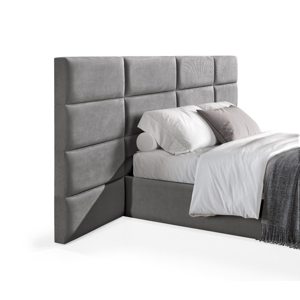 Cama moderna com cabeceira acolchoada cinzenta, lençóis brancos, cobertor cinzento e várias almofadas em tons de cinza e branco, com estrutura estofada no mesmo tecido cinzento.